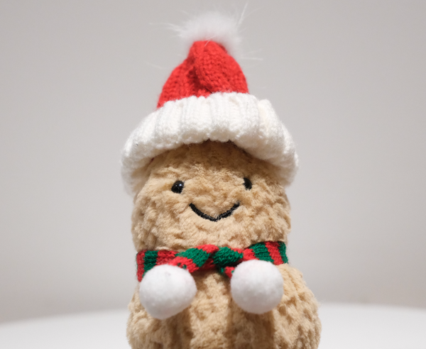 Close-up of the miniature Santa hat and knit scarf detail on the Jellycat Amuseables Peanut plush.