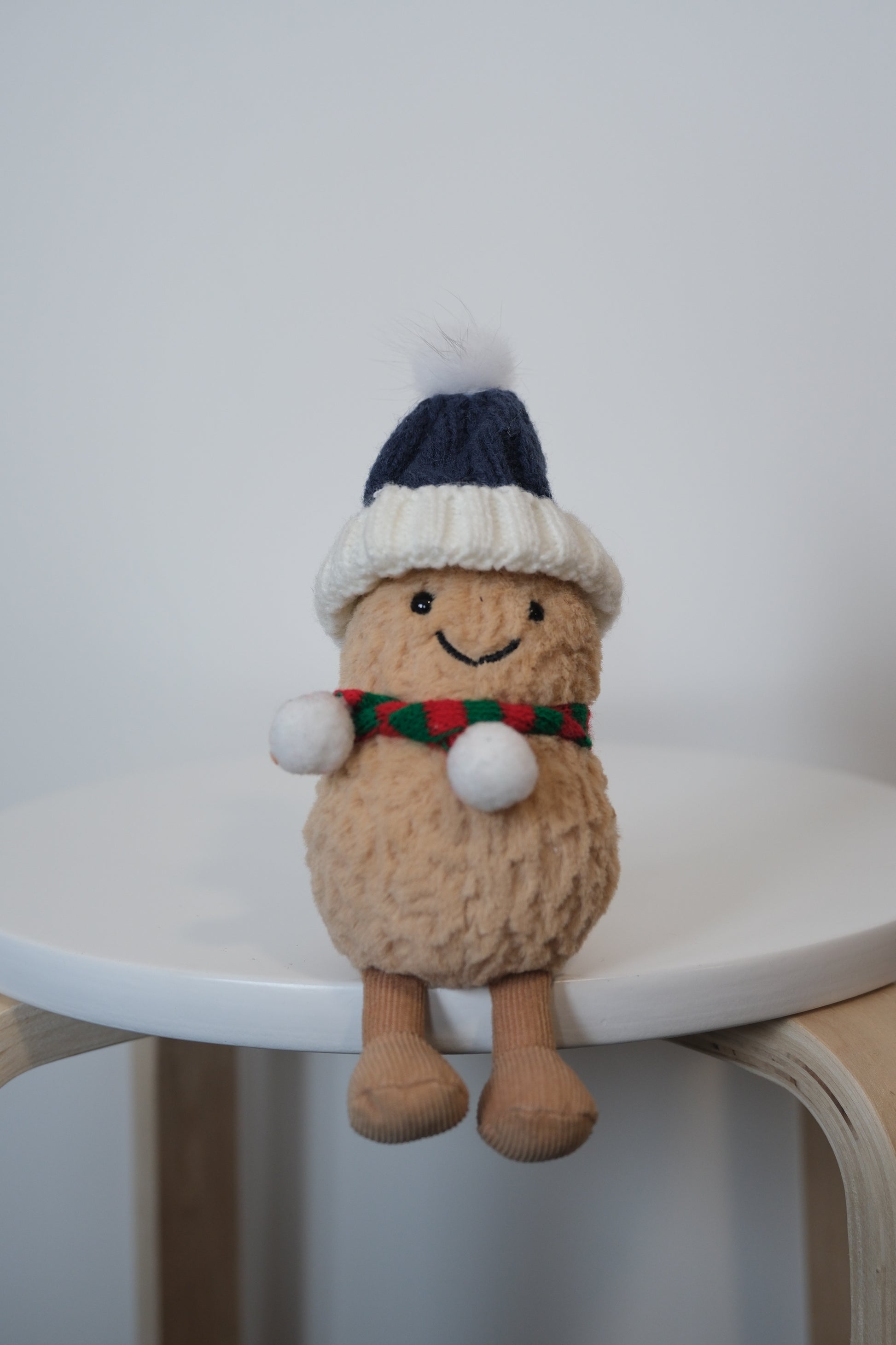 Jellycat Amuseables Peanut plush wearing a 2-piece cozy winter outfit including a knit beanie hat and scarf