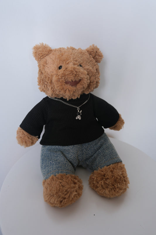 Jellycat Bartholomew Bear wearing a 3-piece punk outfit including a  black sweater, necklace and denim jeans.