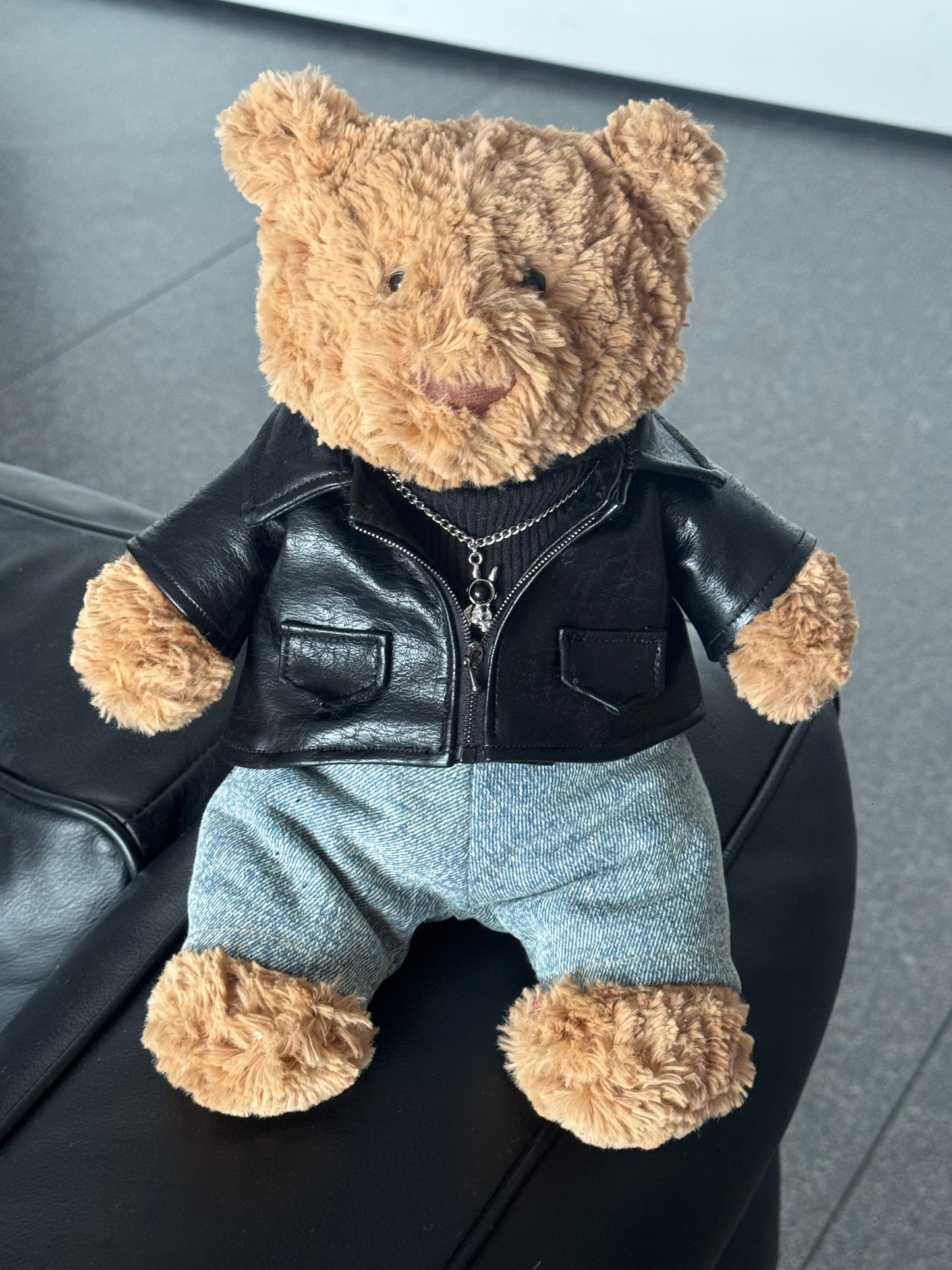 Jellycat Bartholomew Bear wearing a 3-piece punk outfit including a black leather jacket, black sweater, and denim jeans.