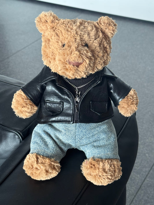 Jellycat Bartholomew Bear wearing a 3-piece punk outfit including a black leather jacket, black sweater, and denim jeans.