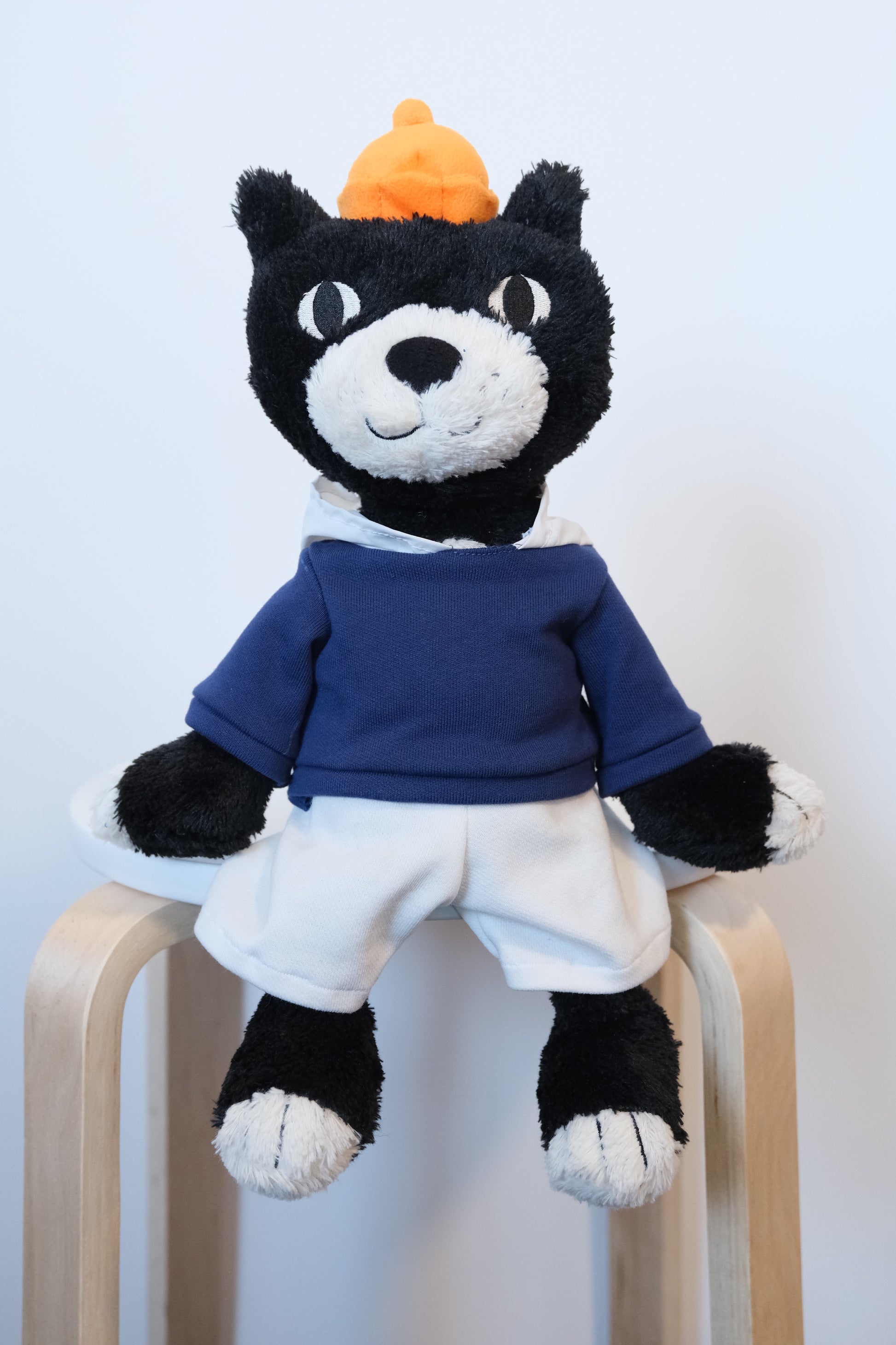 The official Jellycat Jack mascot cat plush wearing a blue streetwear hoodie and high-contrast white pants