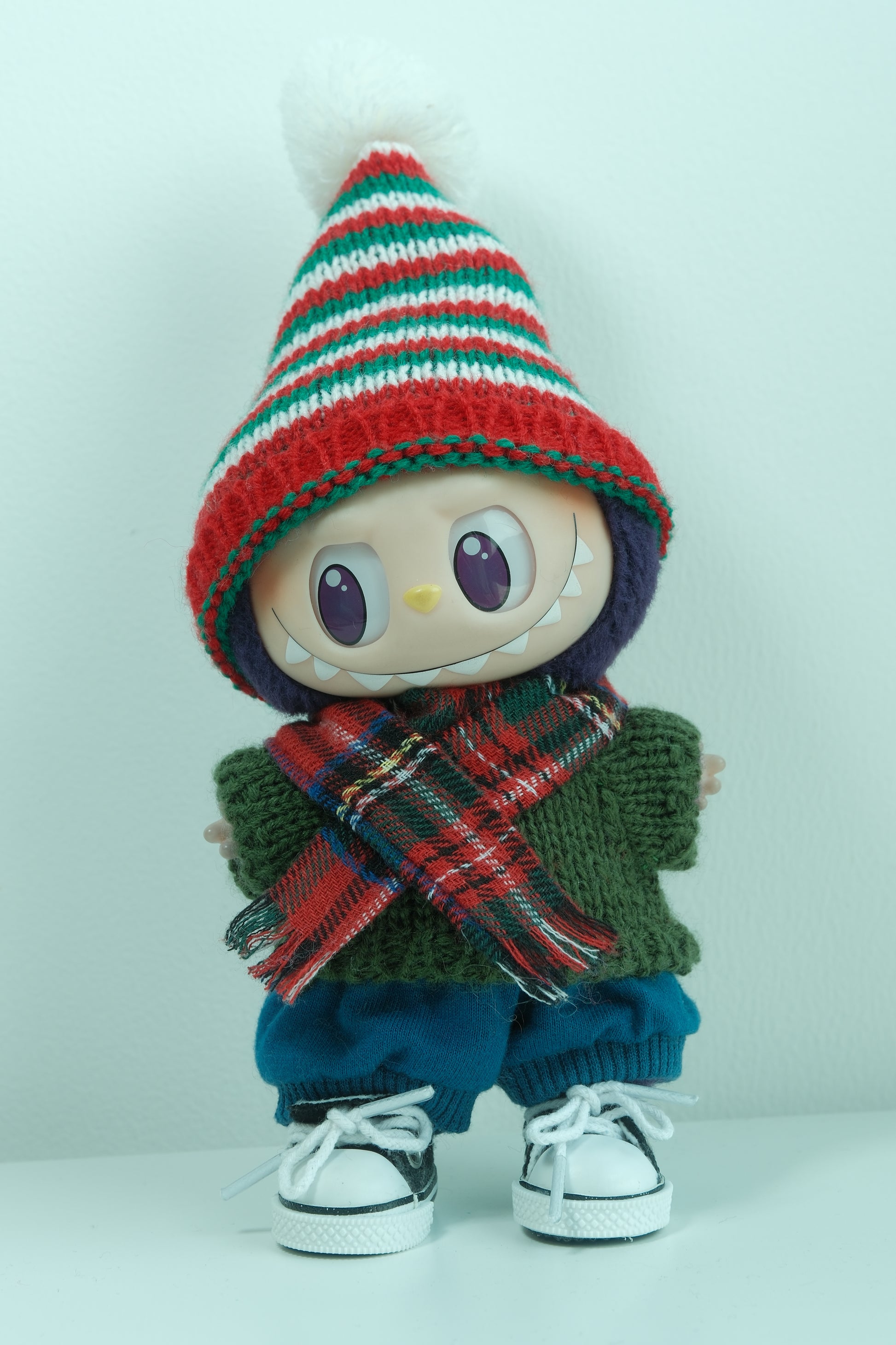 Labubu figure wearing a 5-piece Christmas outfit with a striped elf hat, green knit sweater, plaid scarf, blue pants, and sneakers