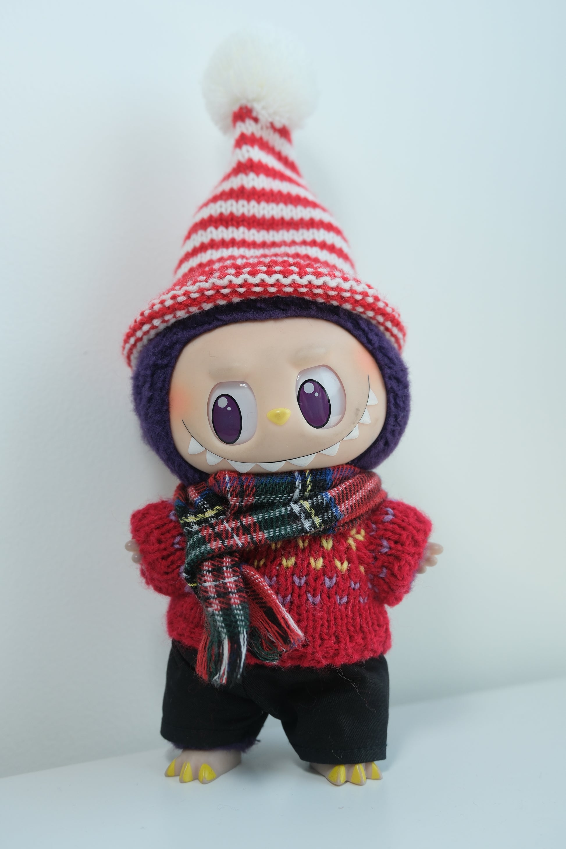 Labubu figure wearing a 4-piece red and white Christmas outfit with a pom-pom beanie, knit sweater, plaid scarf, and black pants