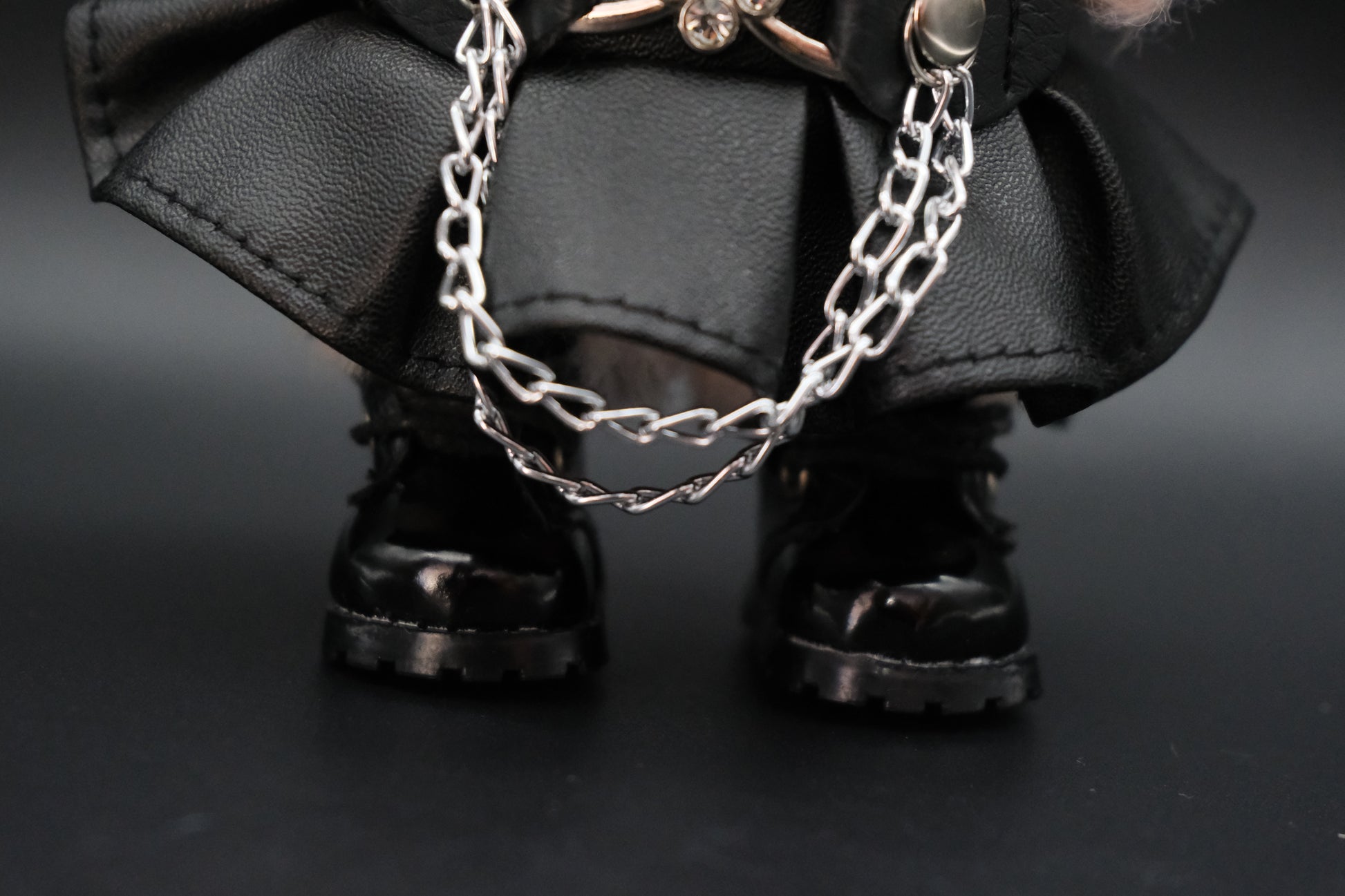 A detailed view of the black faux leather dress, emphasizing the silver chain embellishment and the delicate silver flower-shaped buckle on the straps.