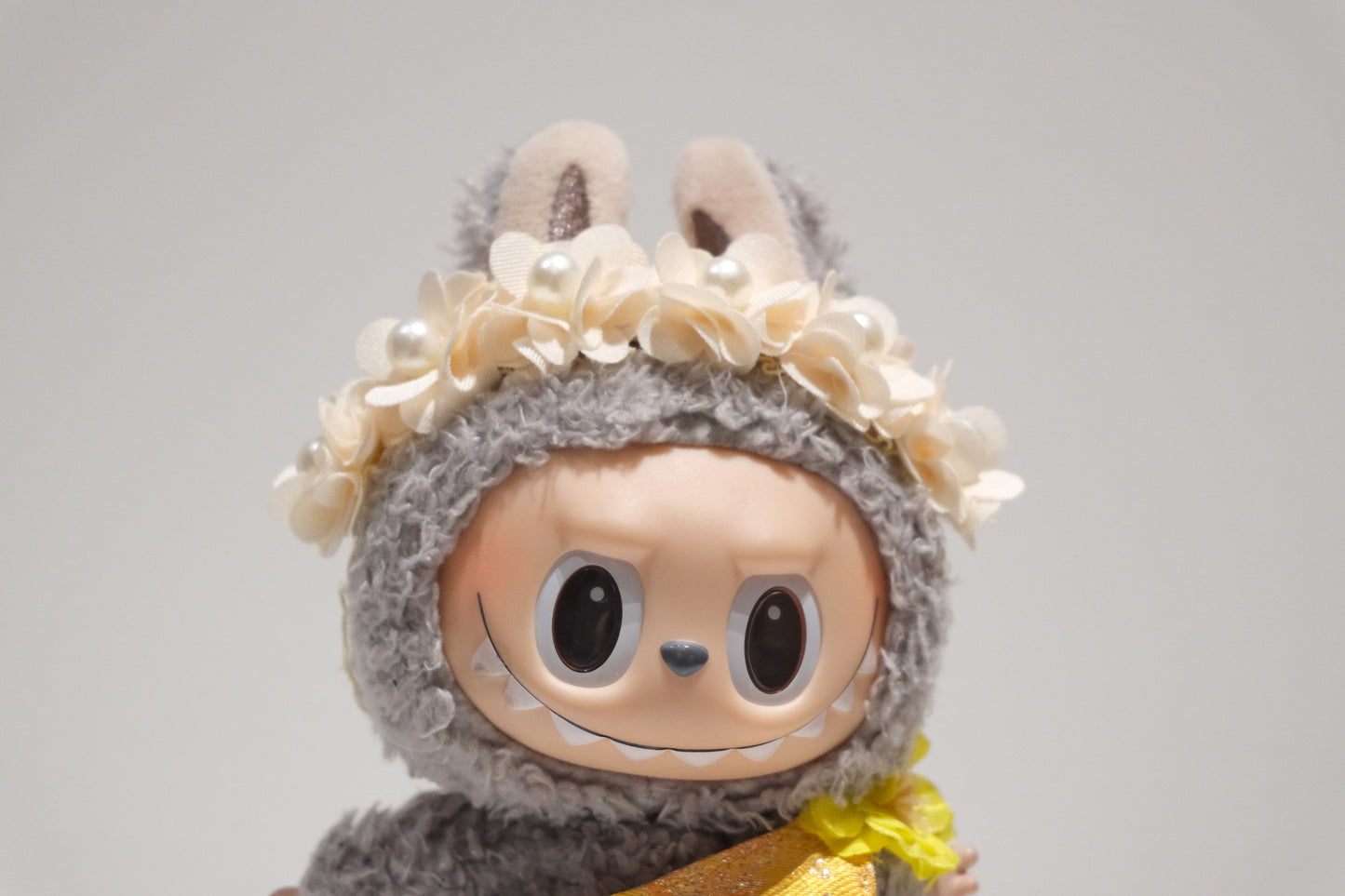 Close-up of The labubu figure's delicate pearl floral crown and shimmering yellow formal dress