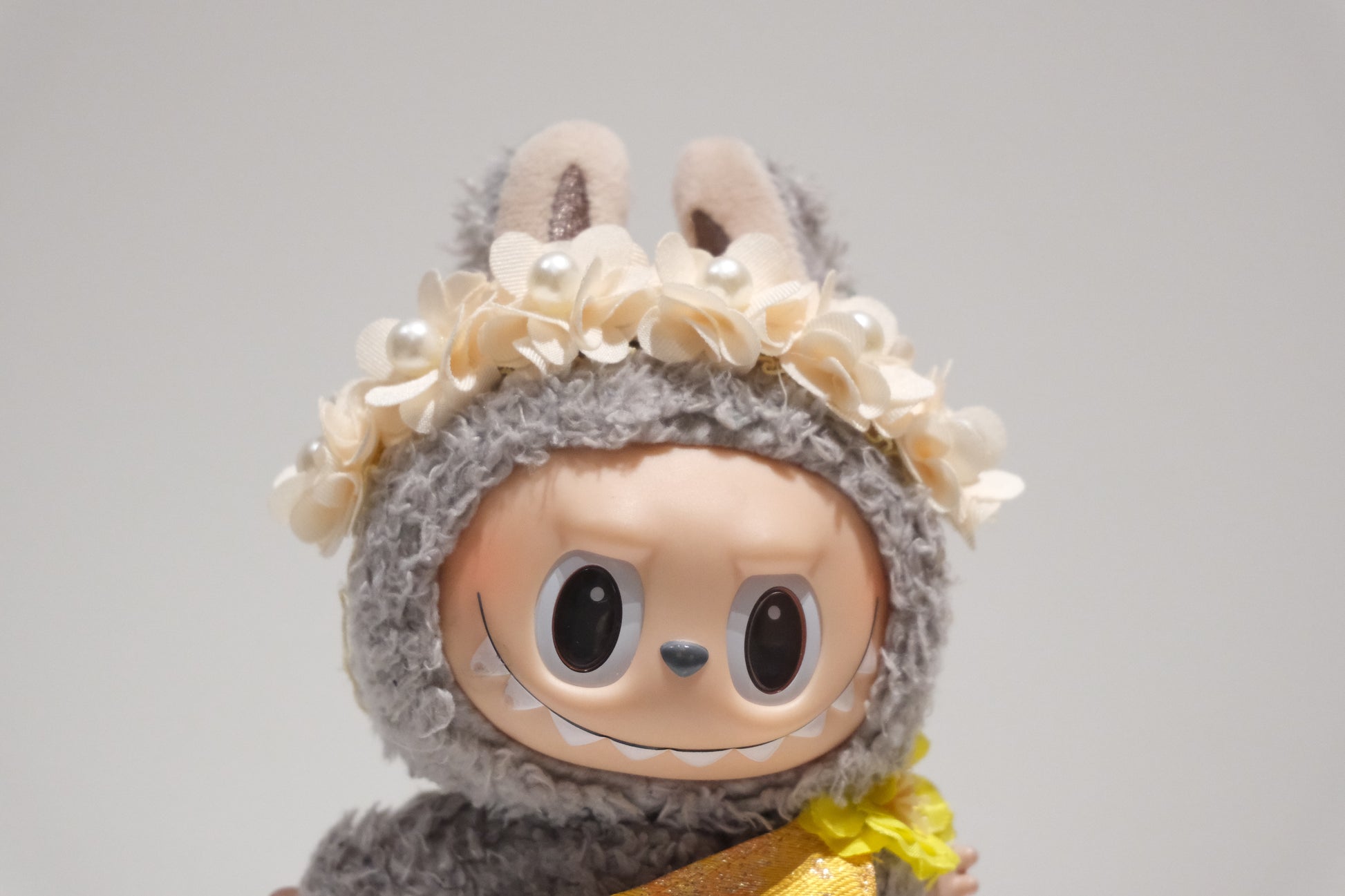 Close-up of The labubu figure's delicate pearl floral crown and shimmering yellow formal dress