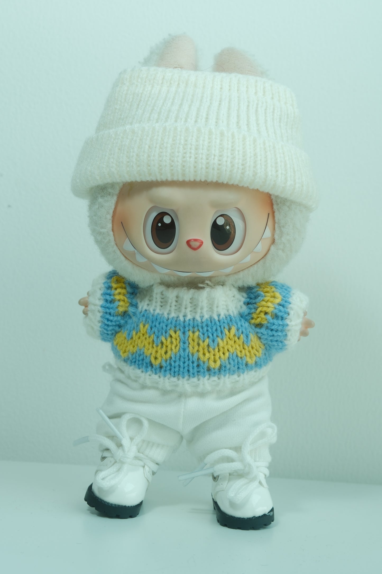 Labubu figure wearing a 4-piece cozy knitwear outfit with a blue and yellow sweater, white beanie, white pants, and white sneakers