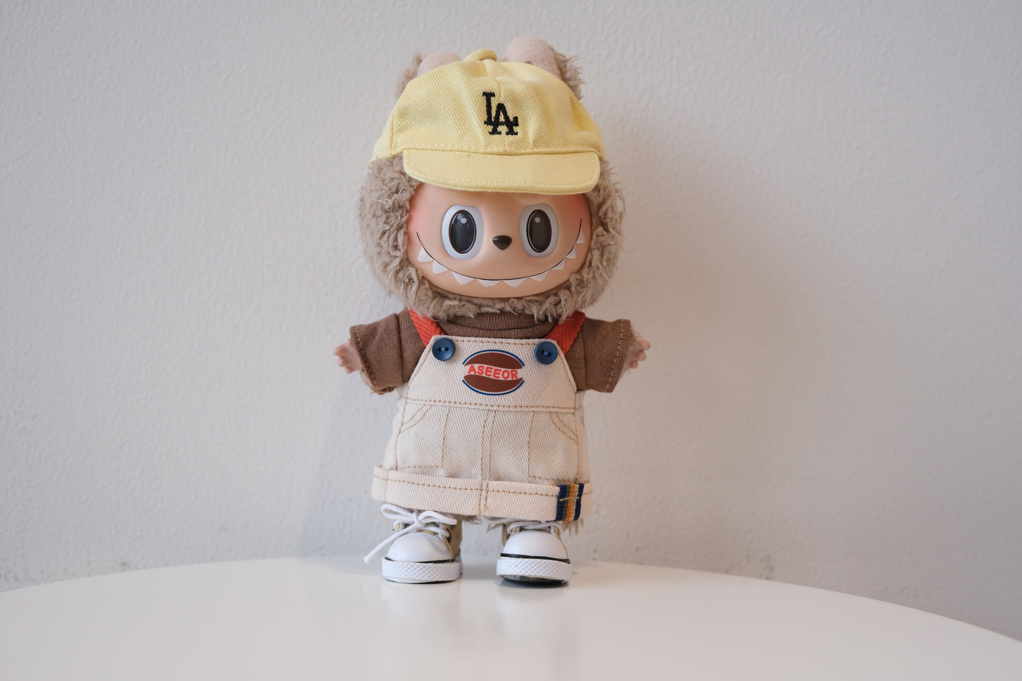 Labubu figure wearing a 4-piece 90s streetwear outfit with denim dungarees, a yellow T-shirt, cap, and sneakers