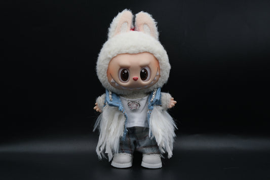 Front view of a Labubu art toy in a unique outfit. The doll wears a light blue denim vest with sparkly rhinestone accents on the shoulders, a white t-shirt, and plaid pants. A white furry, feathery shawl or jacket is layered over the outfit. The doll has  a star-shaped necklace.