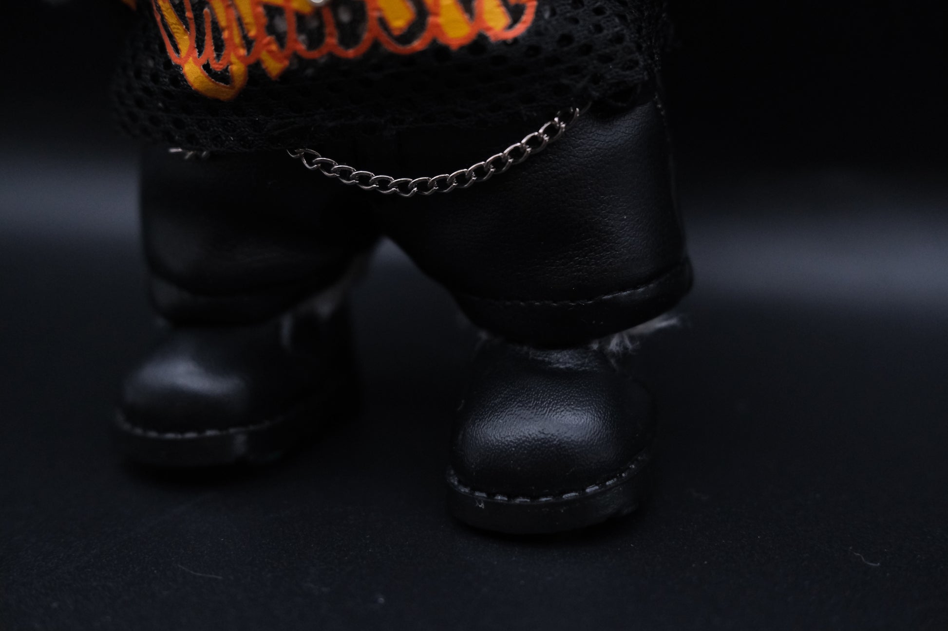 details of a labubu mesh shirt, leather pants, black shoes and cross necklace