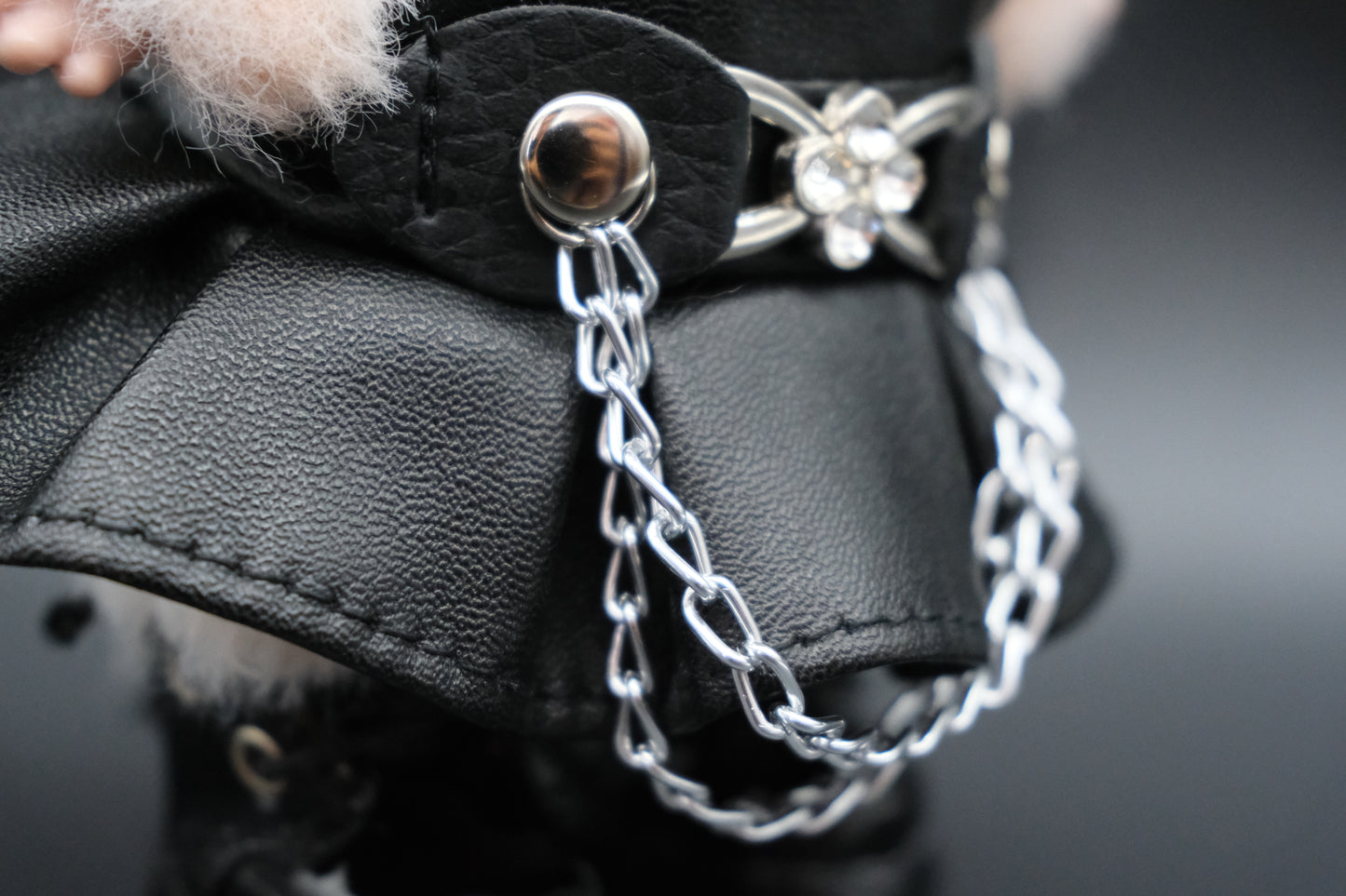 A detailed view of the black faux leather dress, emphasizing the silver chain embellishment and the delicate silver flower-shaped buckle on the straps.