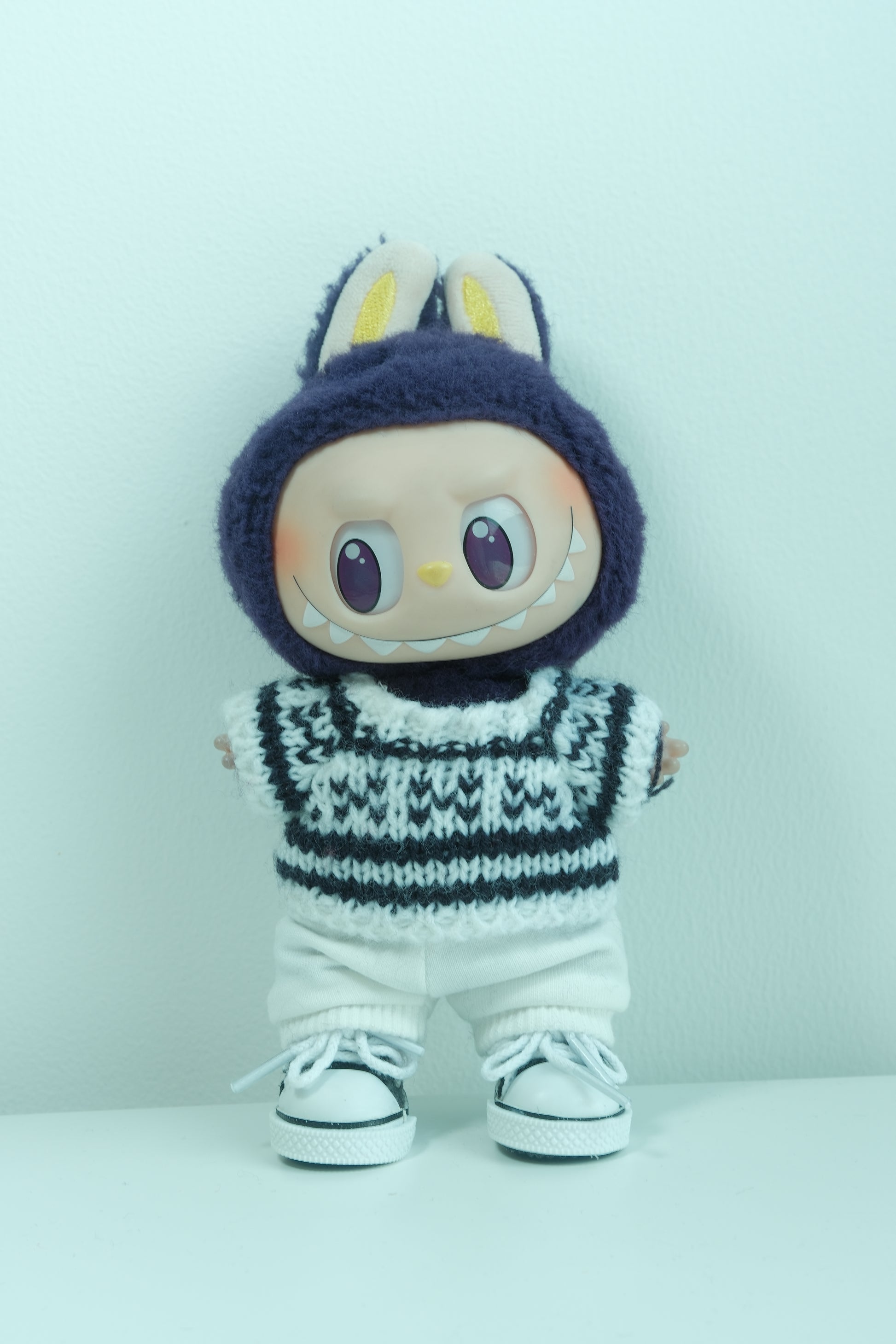 Labubu figure wearing a 3-piece monochromatic winter outfit with a black and white Fair Isle knit sweater, white pants, and sneakers.