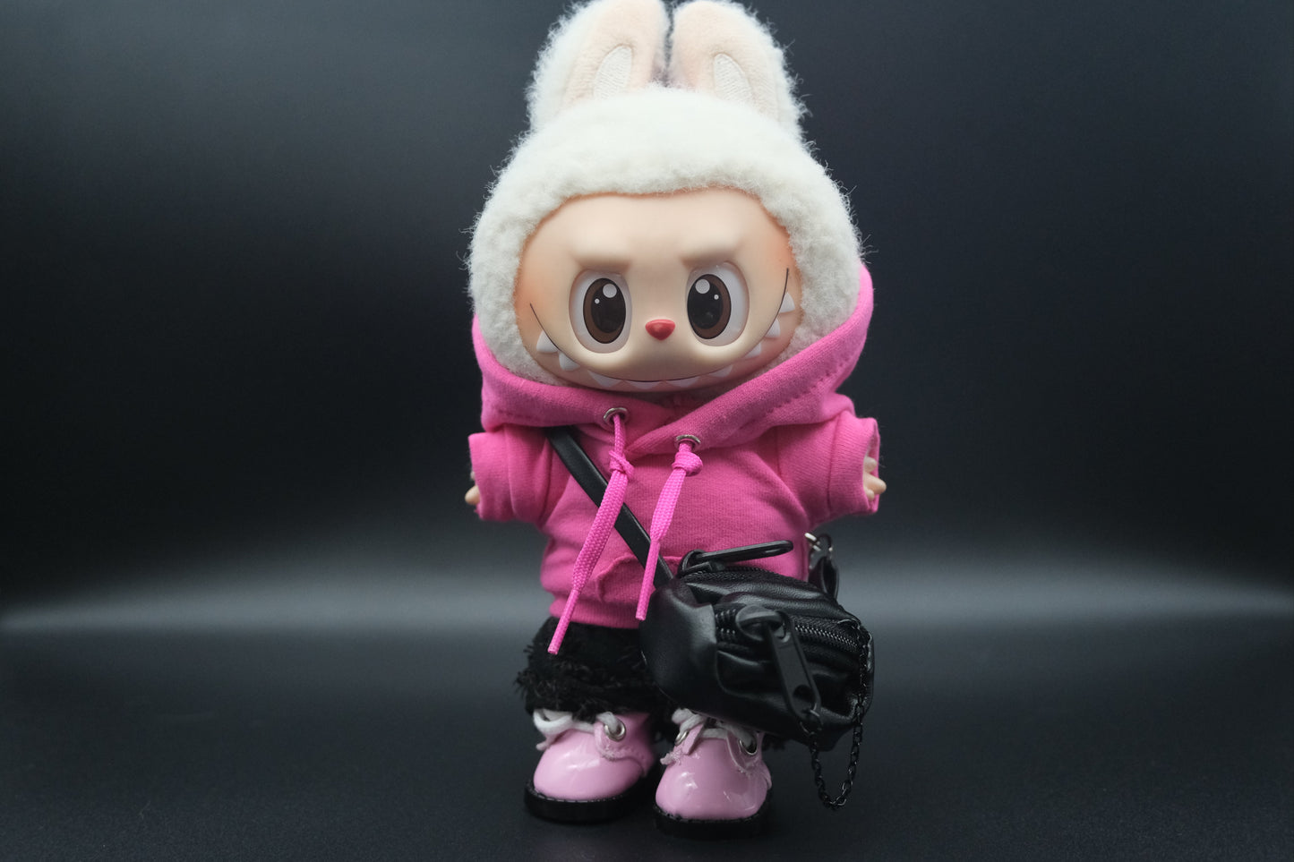 A Labubu figure wearing a pink hoodie, black pants,  crossbody bag and pink sneakers.
