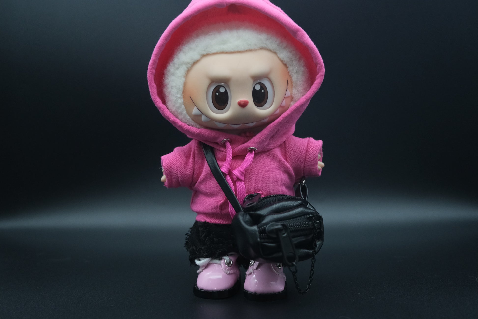 A Labubu figure wearing a pink hoodie, black pants,  crossbody bag and pink sneakers.