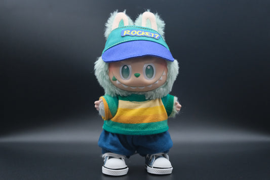 A whimsical Labubu designer toy figure sporting a teal and blue baseball-style cap with a royal blue brim and a yellow "ROCKET?" patch on the front. It's paired with a long-sleeved top featuring bold horizontal stripes in teal, yellow, and white. The figure also wears relaxed-fit blue shorts with a drawstring and classic white sneakers with blue accents and black trim.