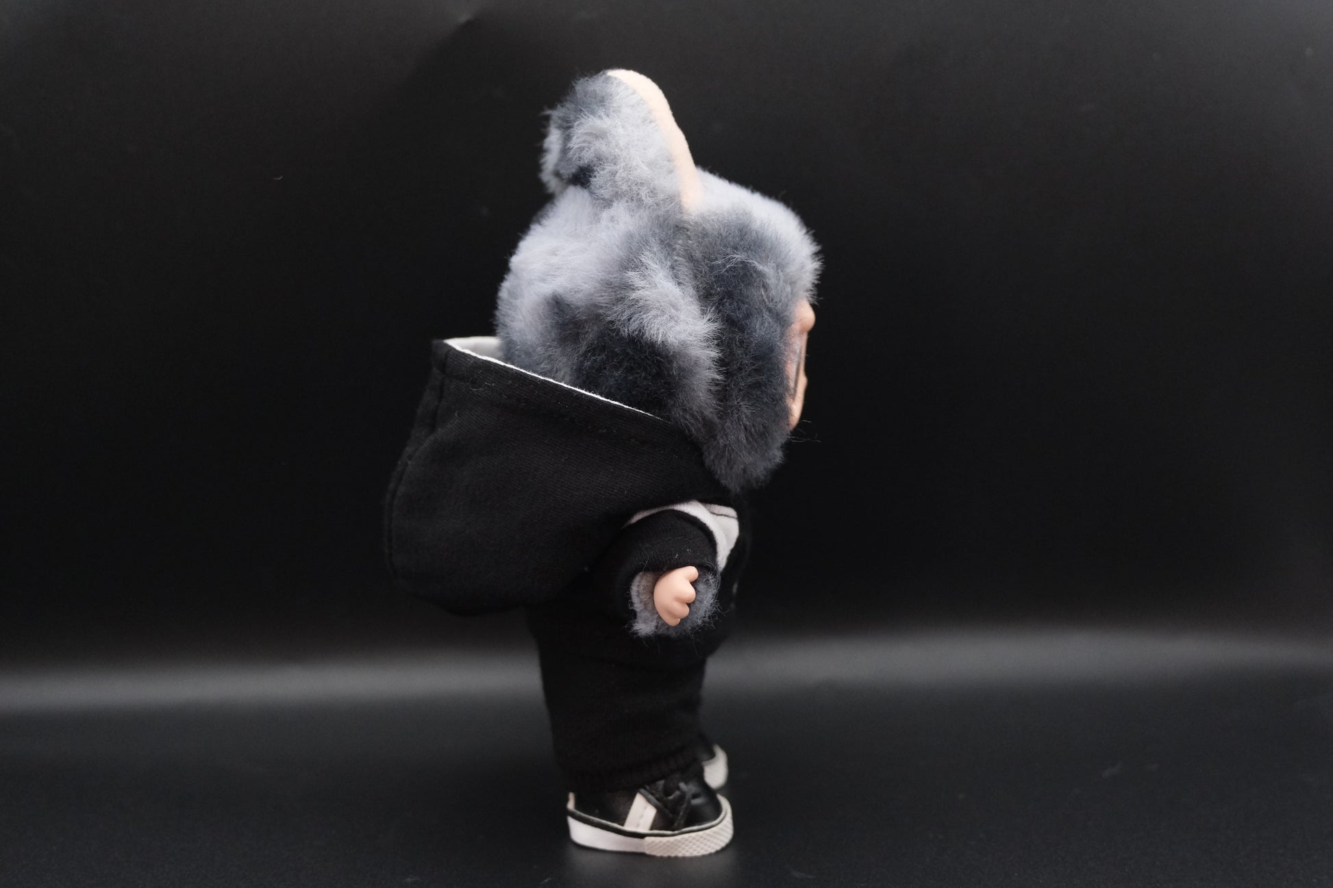 A side view of  trendy Labubu designer toy figure wearing a black and white hoodei, pants and black shoes