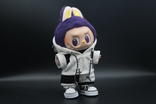 Front view of a Labubu art toy wearing a white hoodie with a skeleton ribcage graphic and a skeleton hand chain on the hood. The toy also wears black and white shorts and white high-top sneakers. Two silver cross necklaces hang from a black and white braided cord.