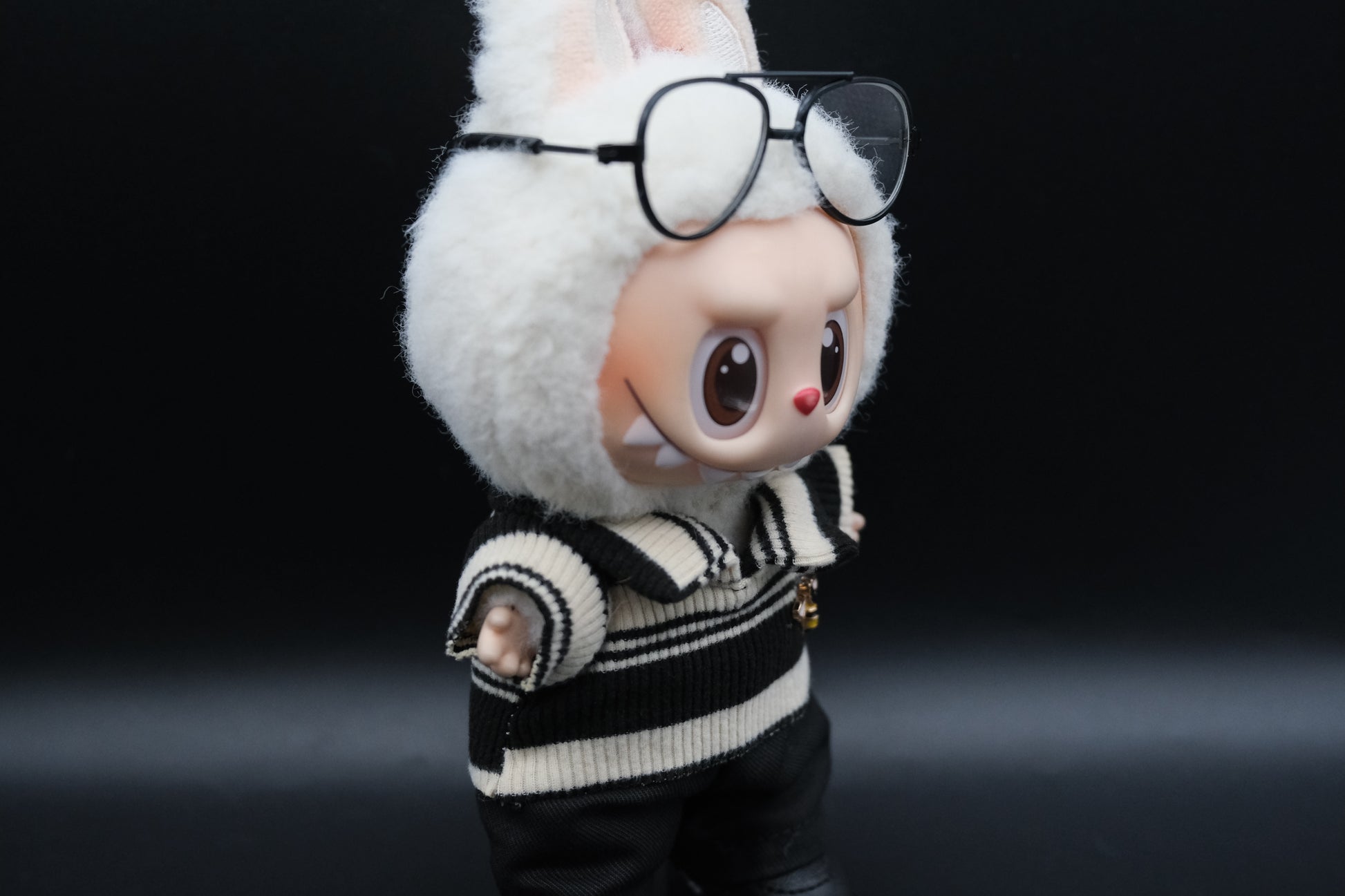 details of A Labubu figure wearing a white  and black color-blocked shirt, black pants and glasses