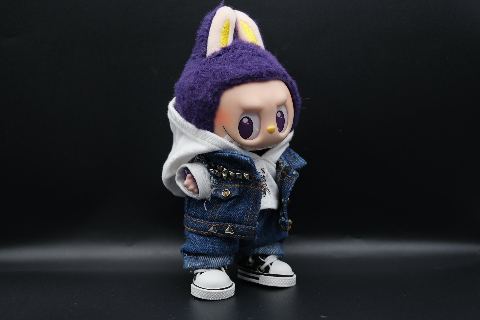 A Labubu designer toy figure showcasing a streetwear look with a white hoodie, a denim jacket, denim jeans and  black sneakers.