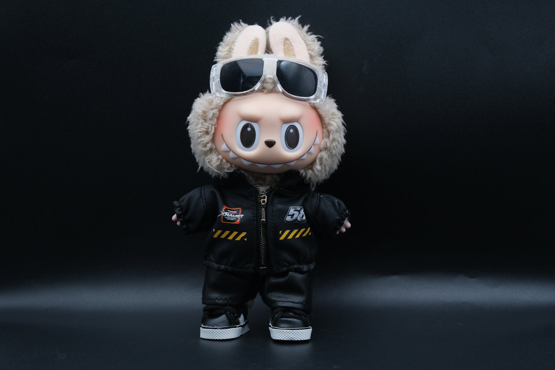 A Labubu designer toy figure in a dark, urban-style outfit, featuring a black leather jacket and pants , sunglasses and a pair of shoes