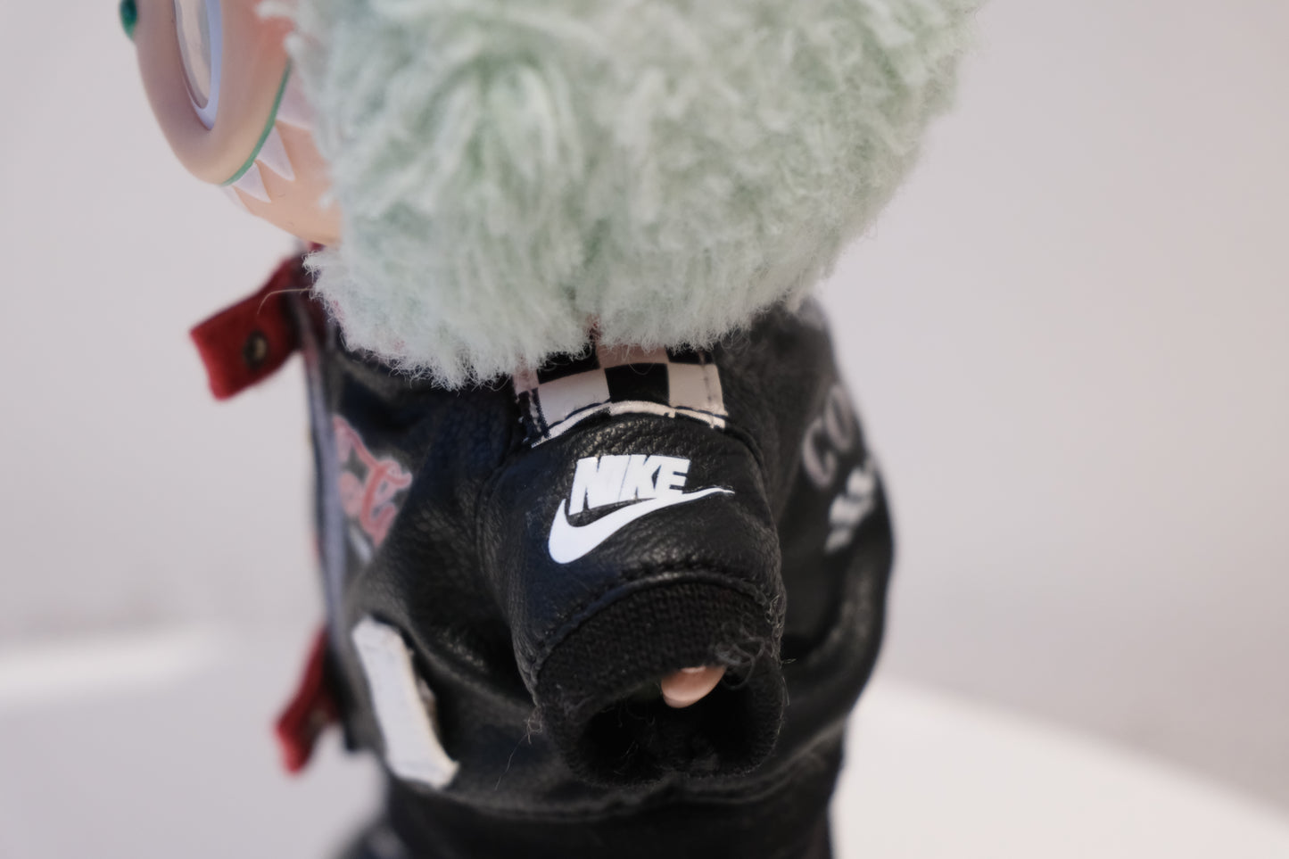 Close-up of a labubu's black leather jacket with a Nike logo on a white background