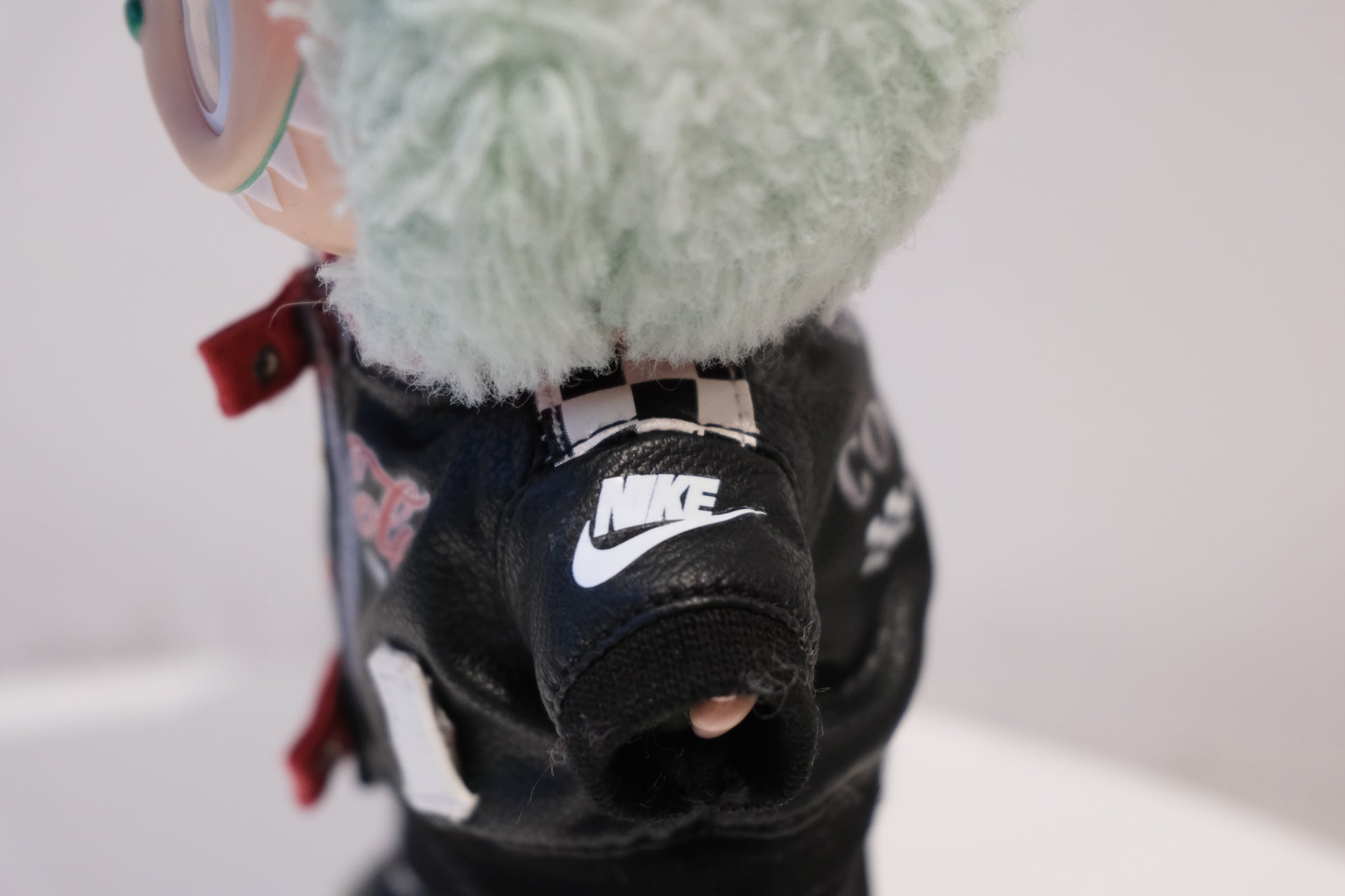 Close-up of a labubu's black leather jacket with a Nike logo on a white background