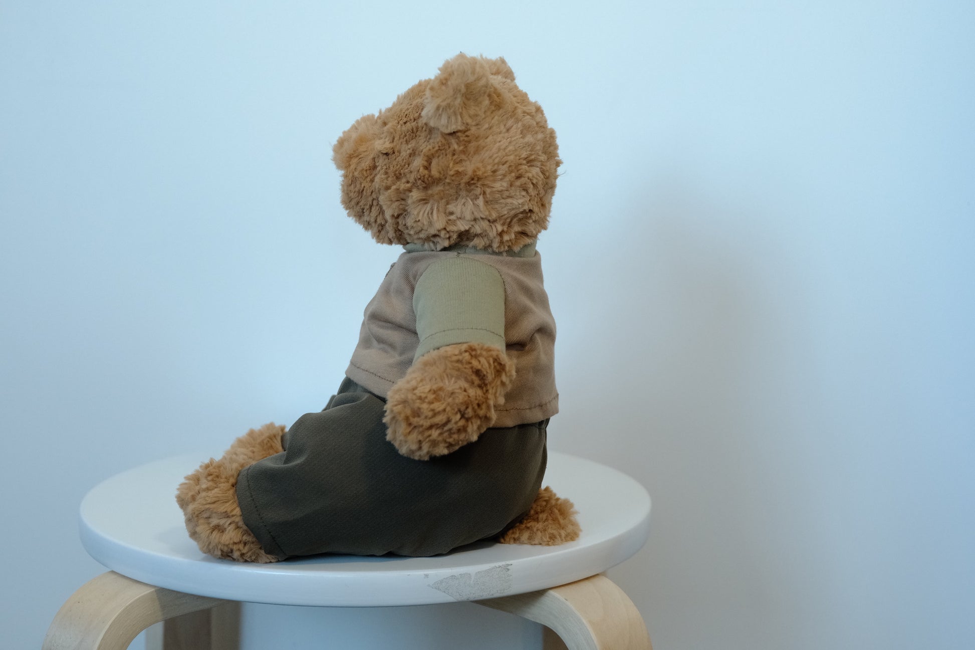 side view of Jellycat Bartholomew Bear plush wearing a 2-piece casual outfit with a gray T-shirt and navy blue pants.