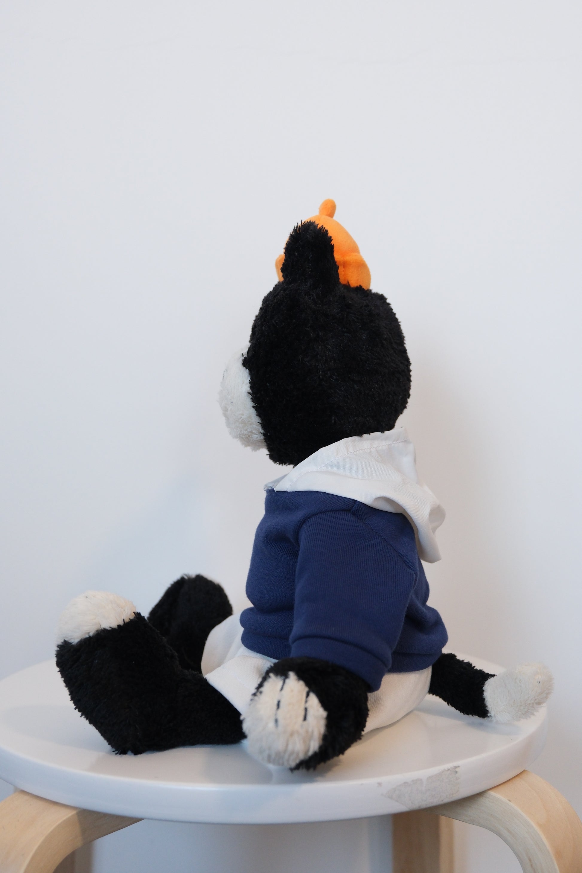 side view of Jellycat Jack mascot cat plush wearing a blue streetwear hoodie and high-contrast white pants