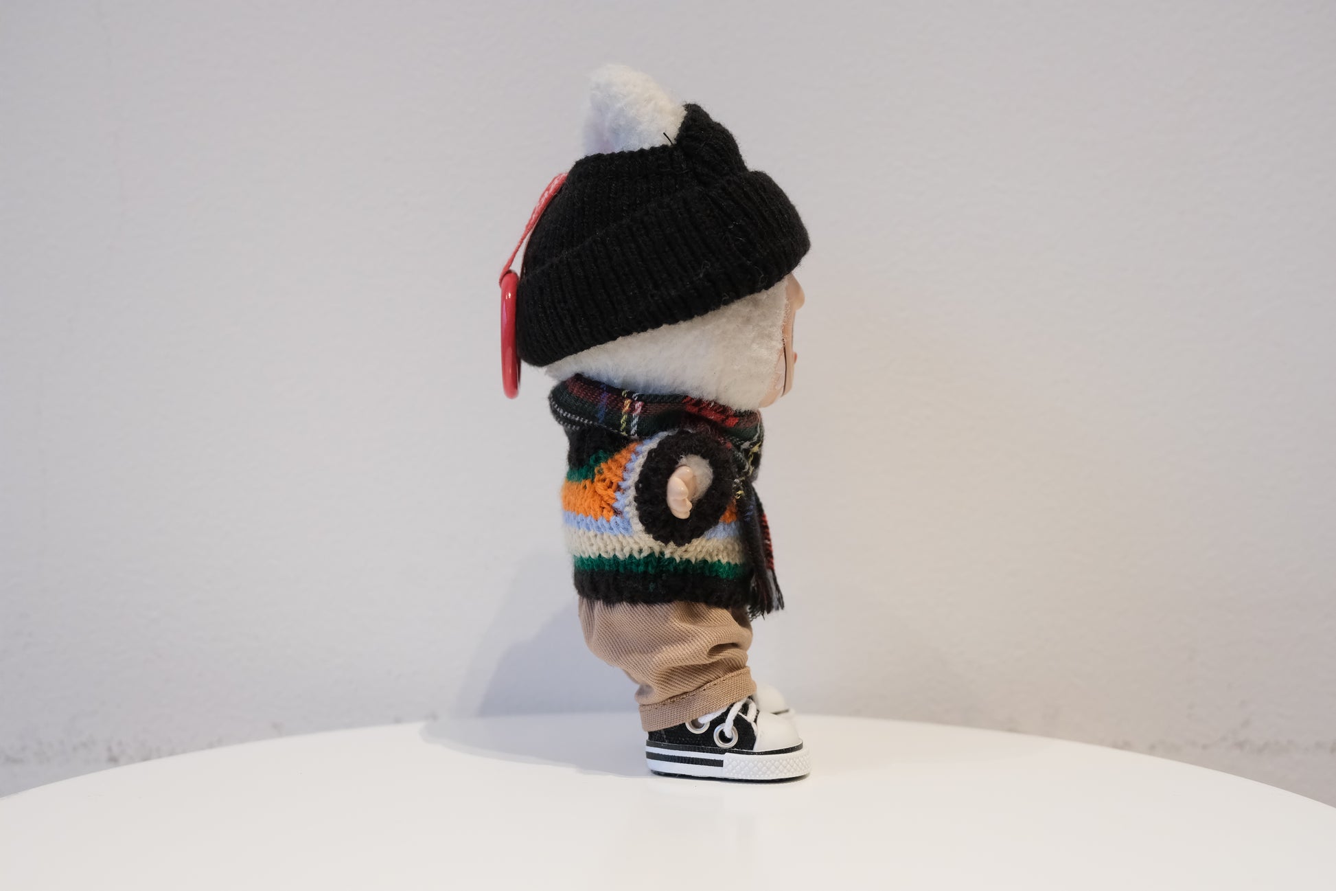 side view of labubu wearing a colorful sweater, black beanie, and shoes