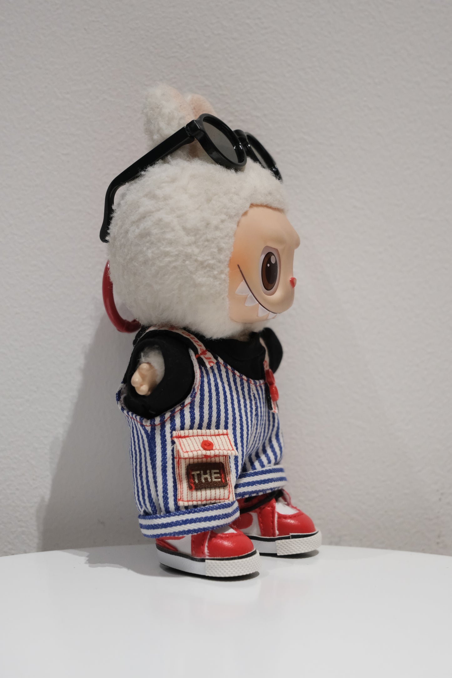 side view of Labubu figure wearing a 4-piece retro streetwear outfit with blue and white striped dungarees, sunglasses, and red high-top sneakers