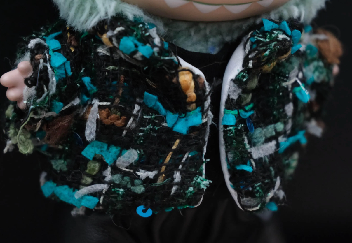 side view of LABUBU plush doll wearing a handmade black tweed jacket with blue and green threads