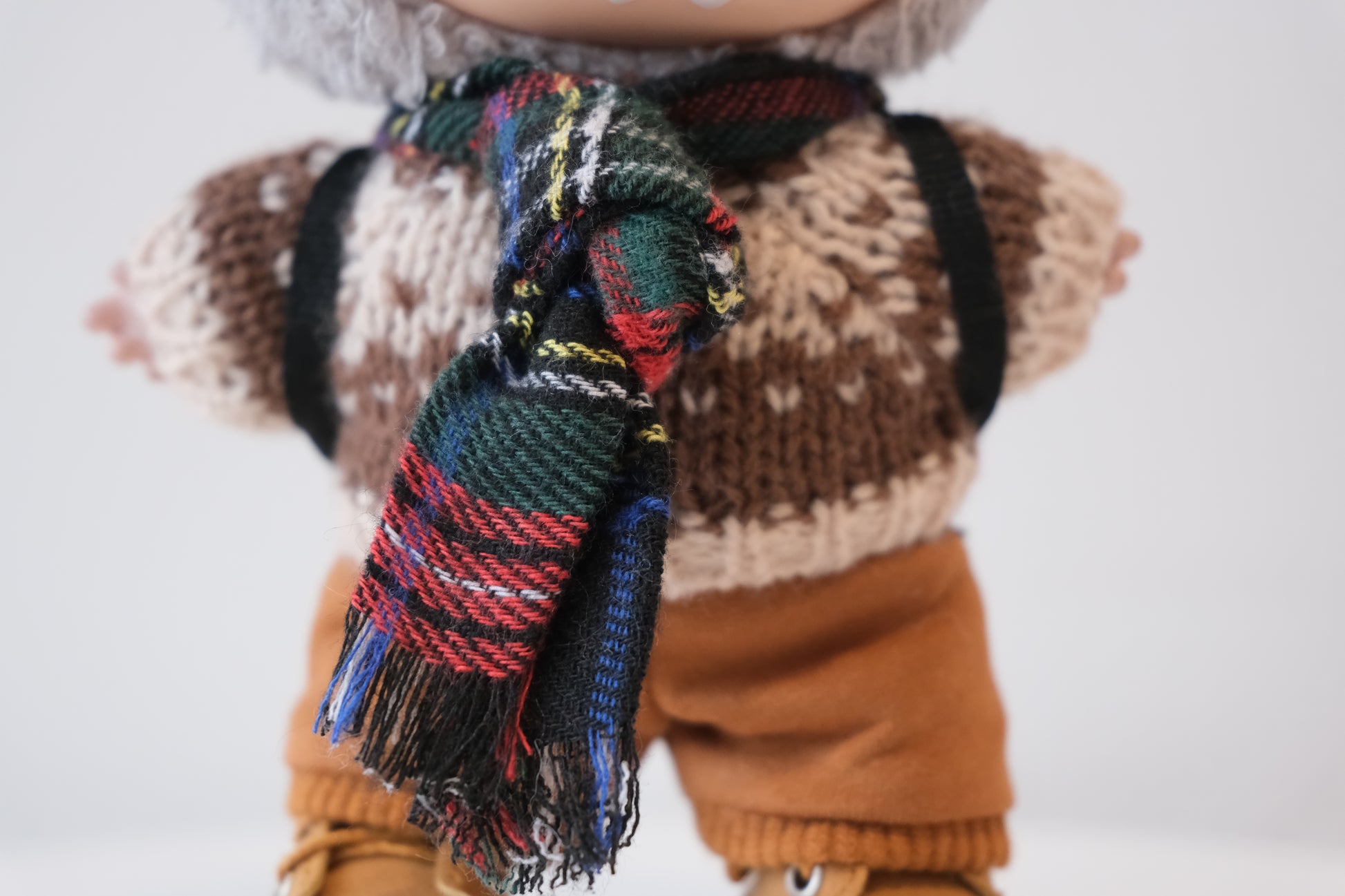 Close-up of The labubu figure's tartan scarf and chunky knit sweater.