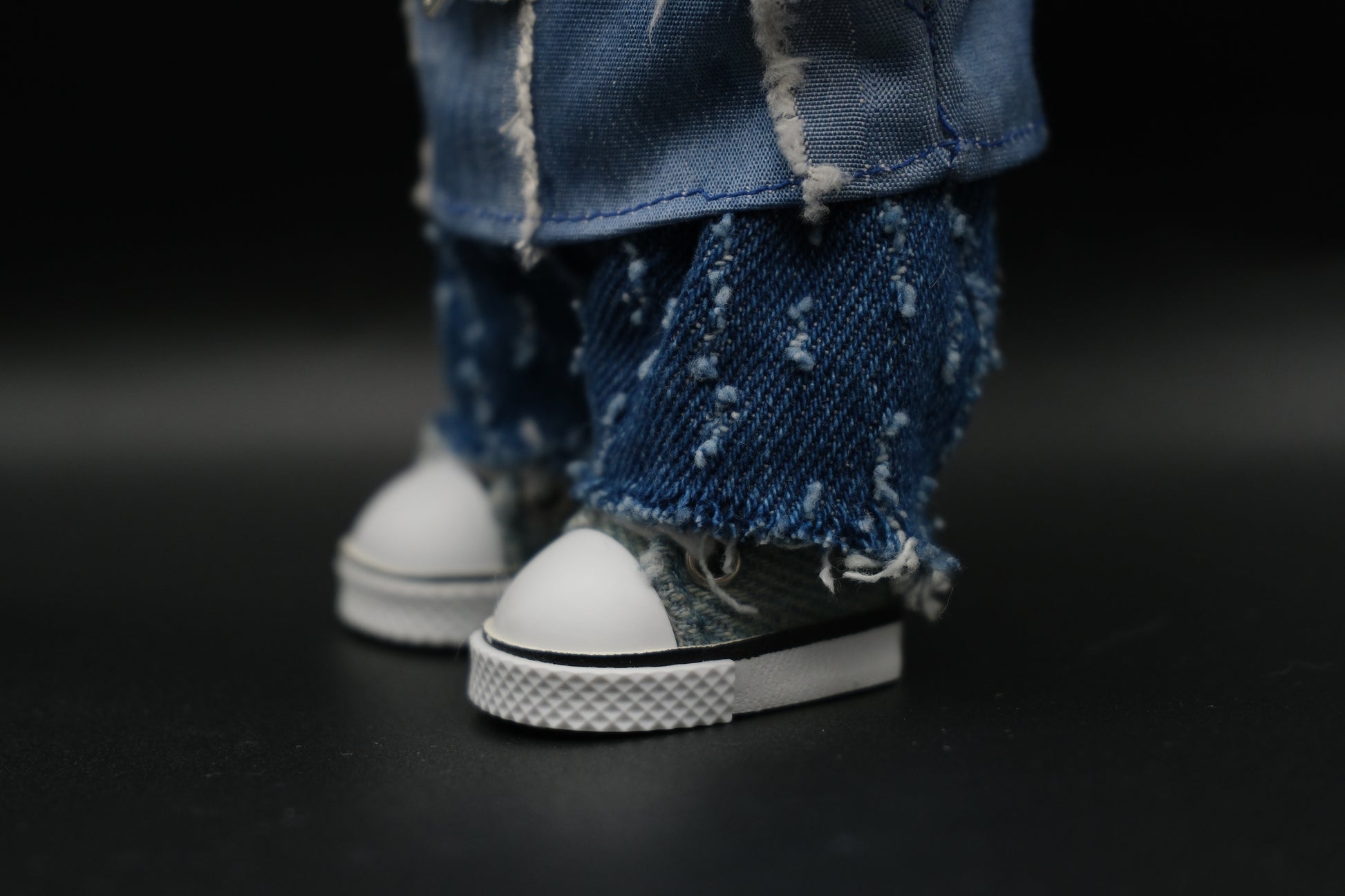 Close-up of a Labubu figure's distressed denim shorts and gray and white sneakers with white laces and soles.