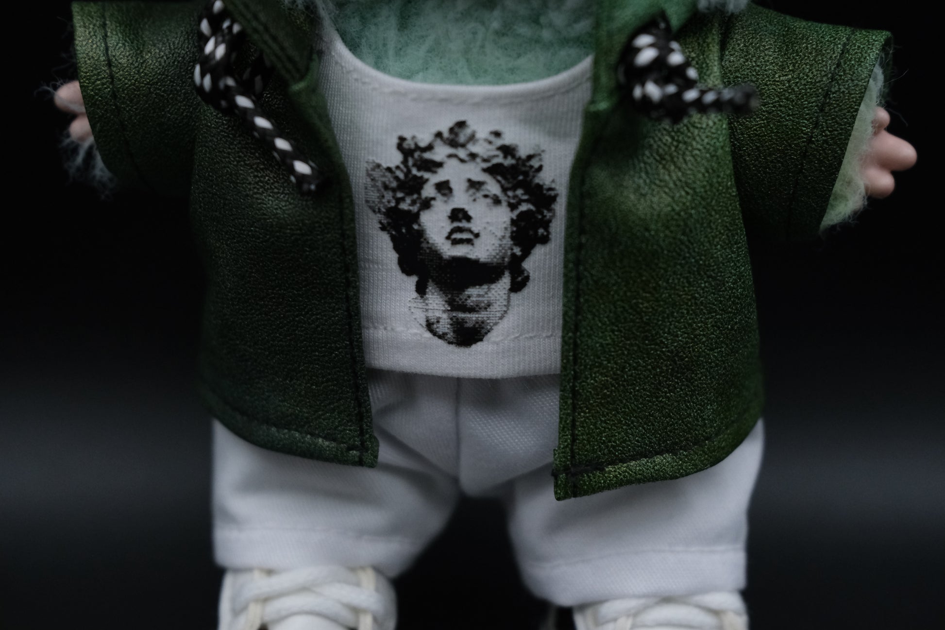 close up of A Labubu's  green leather jacket, white t-shirt and white pants