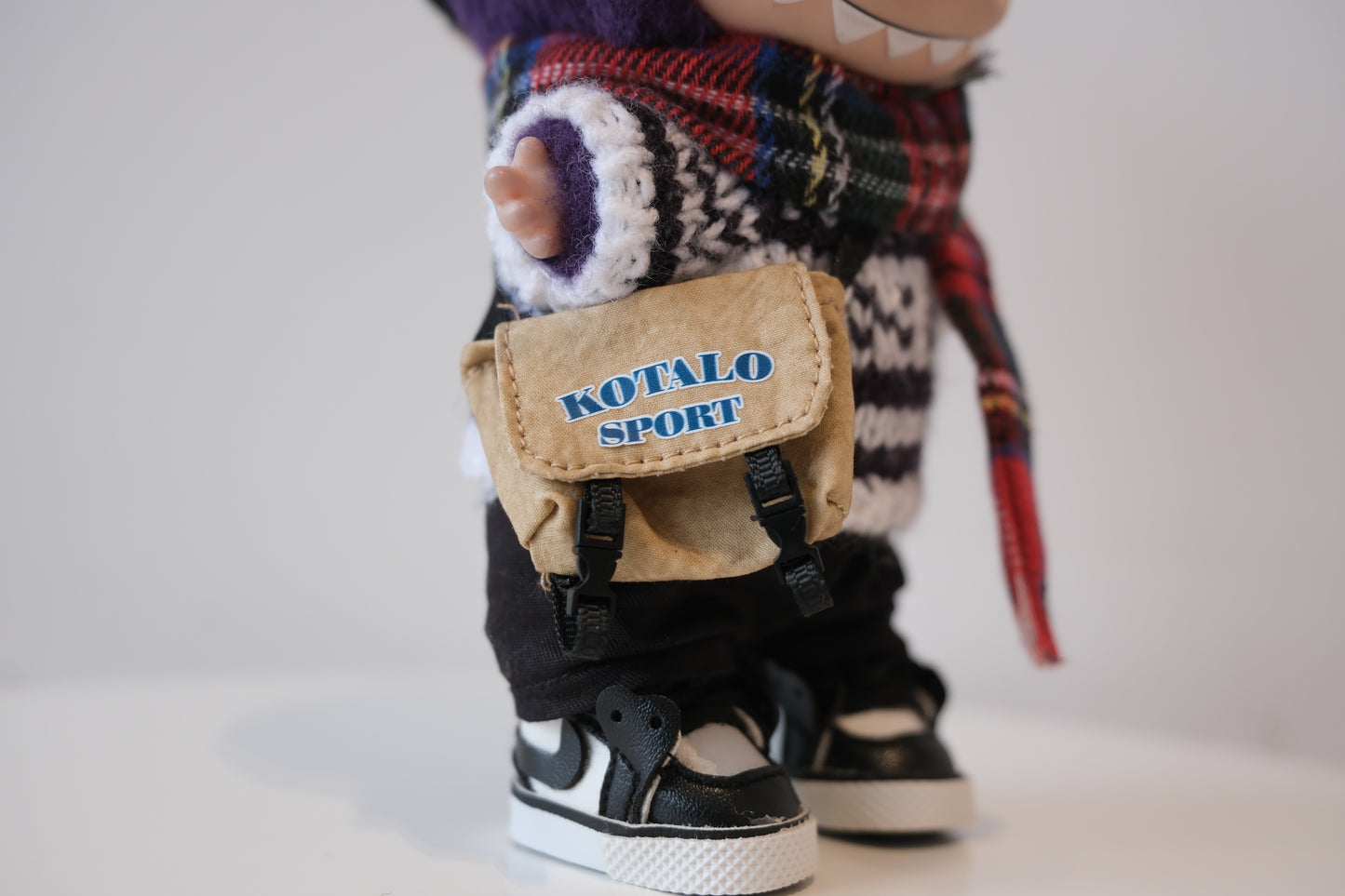 Close-up of The labubu figure's sporty crossbody bag and miniature black and white high-top sneakers.