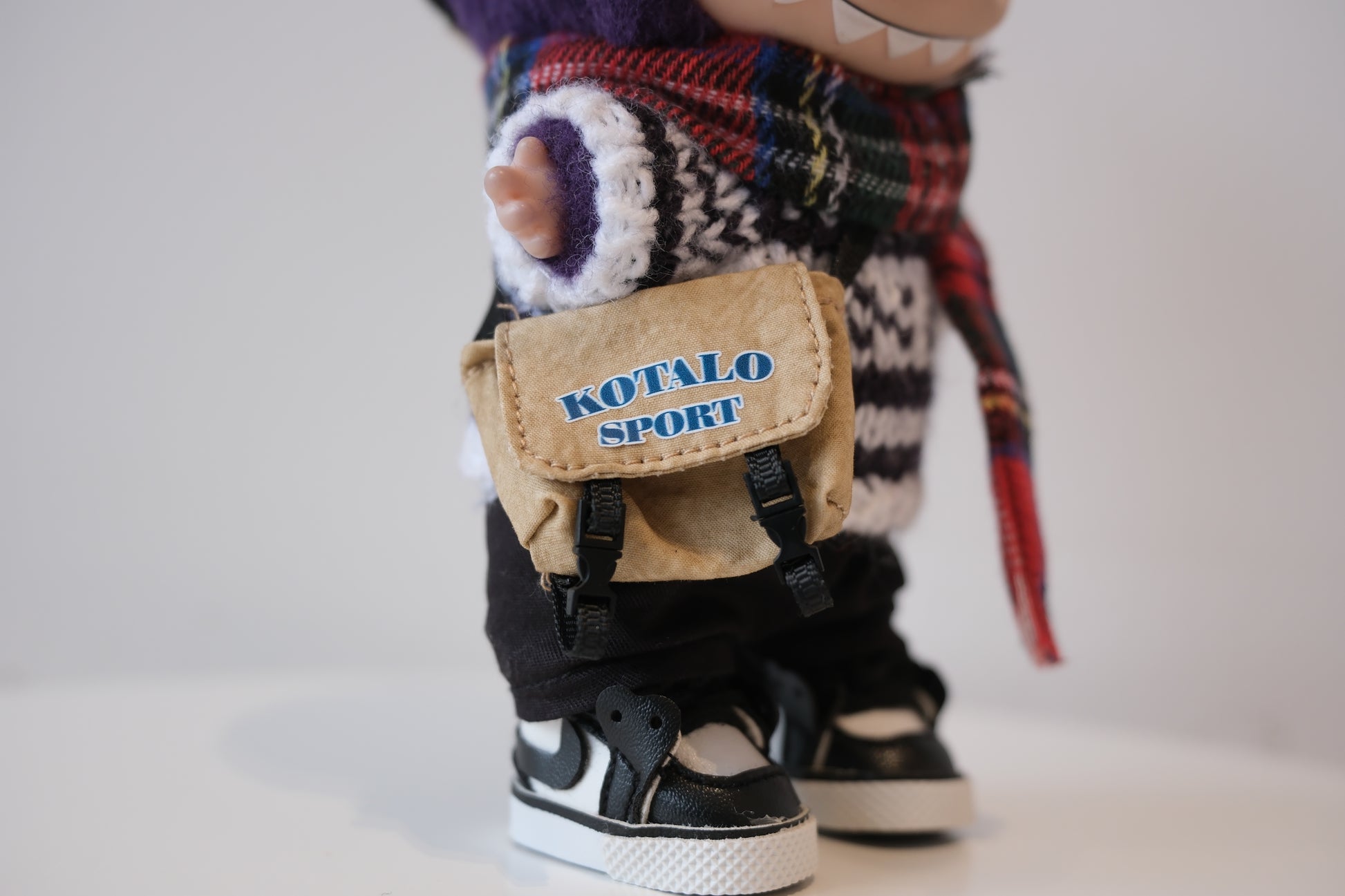 Close-up of The labubu figure's sporty crossbody bag and miniature black and white high-top sneakers.