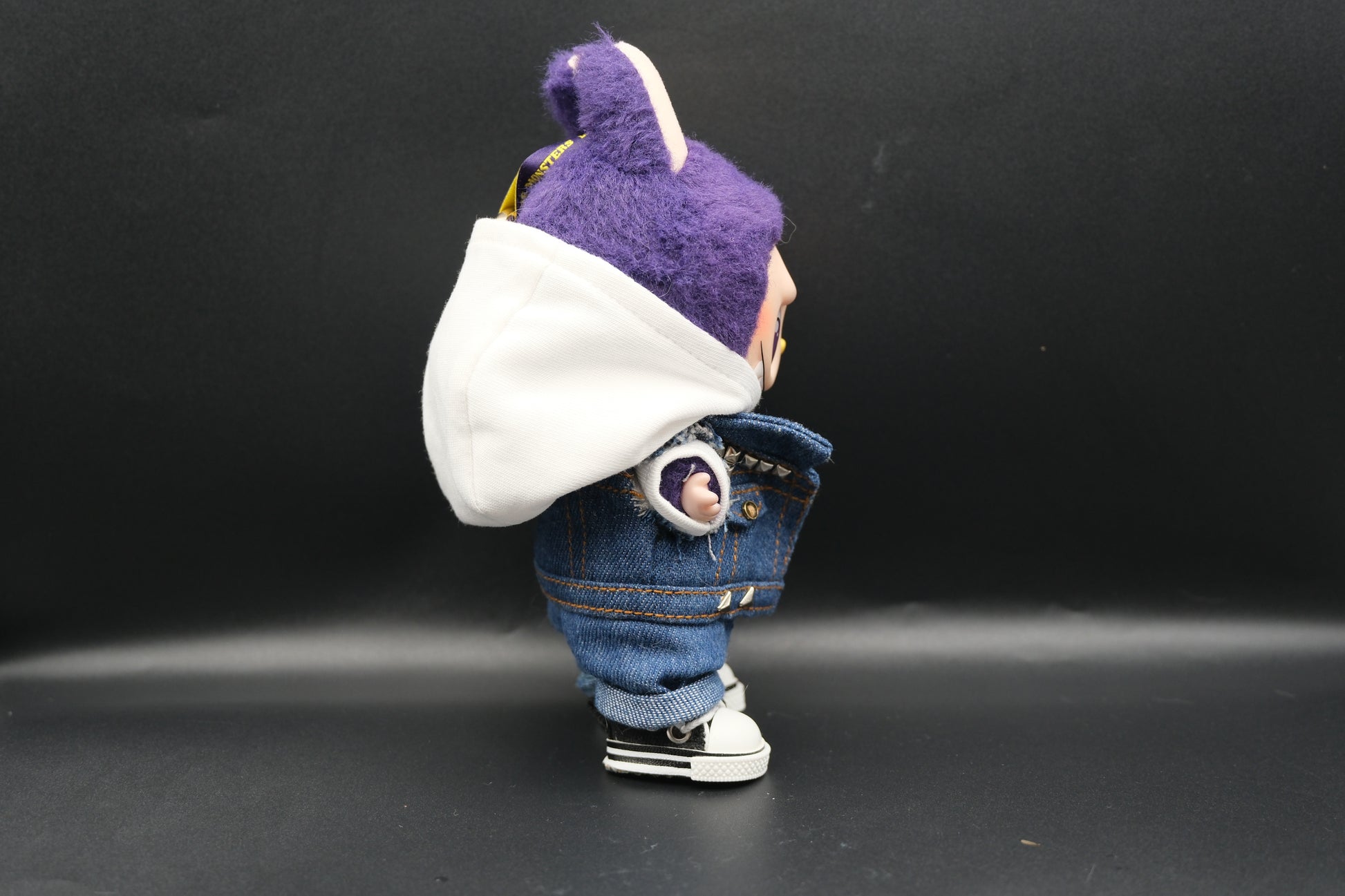 A Labubu designer toy figure showcasing a streetwear look with a white hoodie, a denim jacket, denim jeans and  black sneakers.
