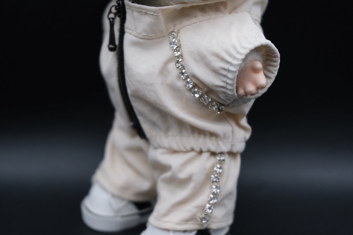 A close- up of  Labubu figure wearing a white zippered jacket, white pants and and white sneakers.